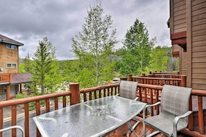 A wooden deck with a glass table and chairs, surrounded by a wooden railing, overlooking a forested area. - Downtown Winter Park Townhouse 3 Mi to Ski Resort! (Winter Park)