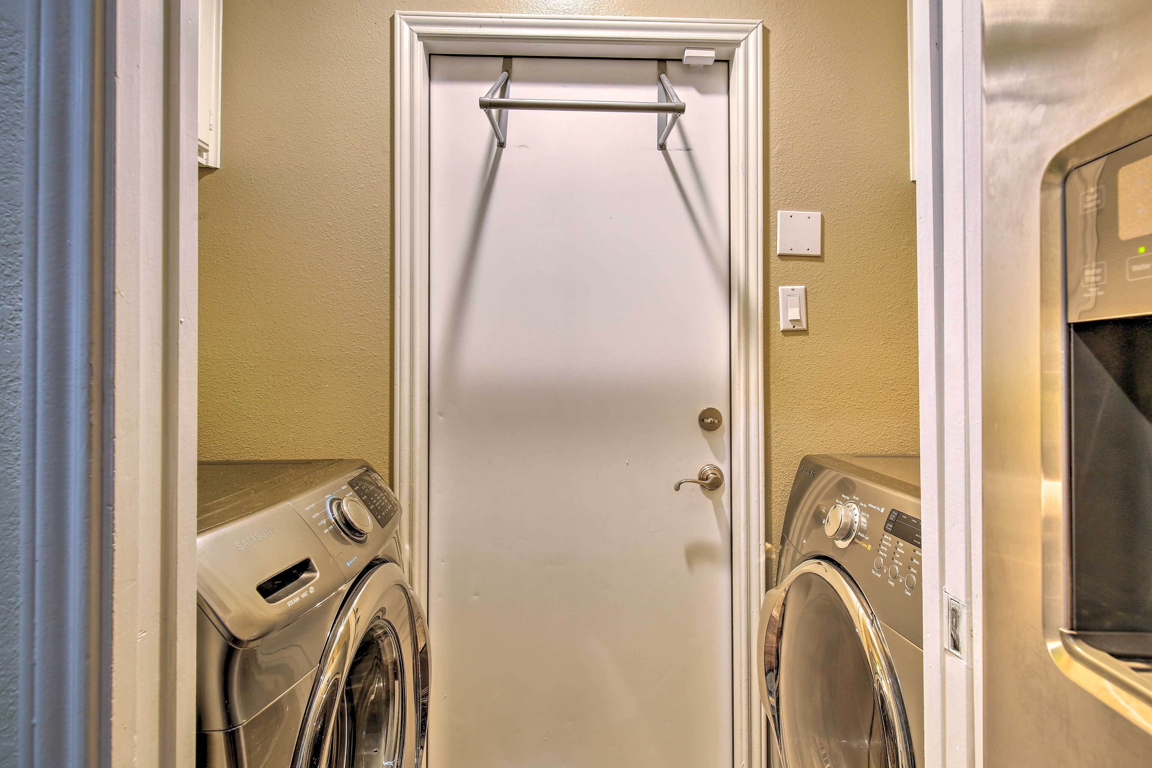A laundry room with two front-loading washing machines and a door with a towel rack above it.