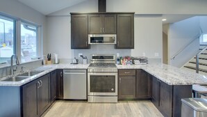 Une cuisine moderne avec des meubles de couleur sombre, des appareils électroménagers en acier inoxydable et un plan de travail en granit.