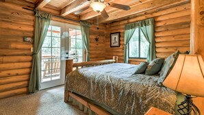 Un dormitorio tipo cabaña de madera con una cama, un ventilador de techo y una ventana con cortinas.