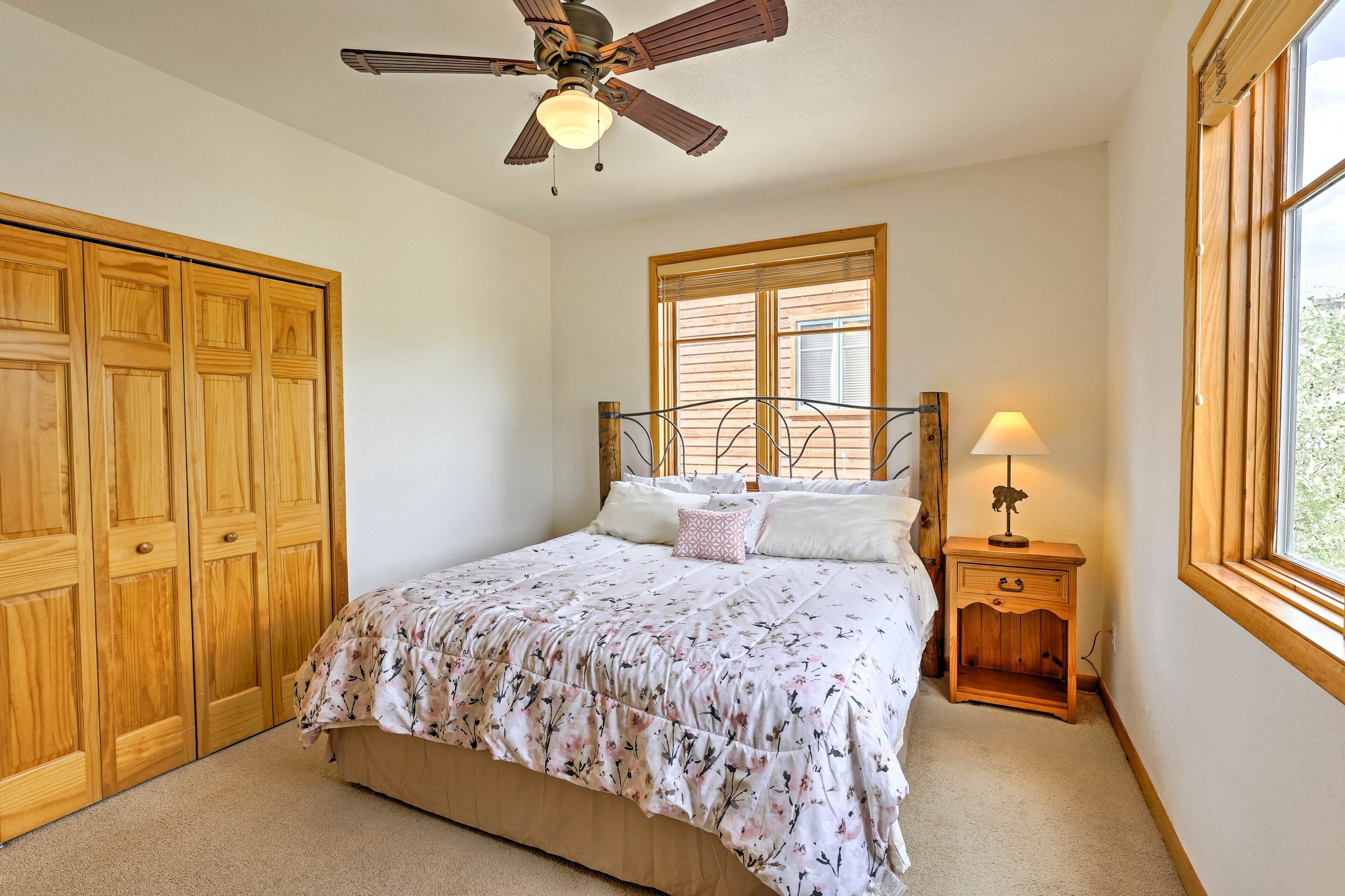 A bedroom with a bed, wooden wardrobe, ceiling fan, window, and nightstand with a lamp.