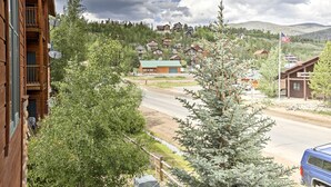A wooden cabin with a balcony, a small building with a green roof, and a view of a mountain range. - 7 Mi to National Park: Grand Lake Condo w/ Deck! (Grand Lake)
