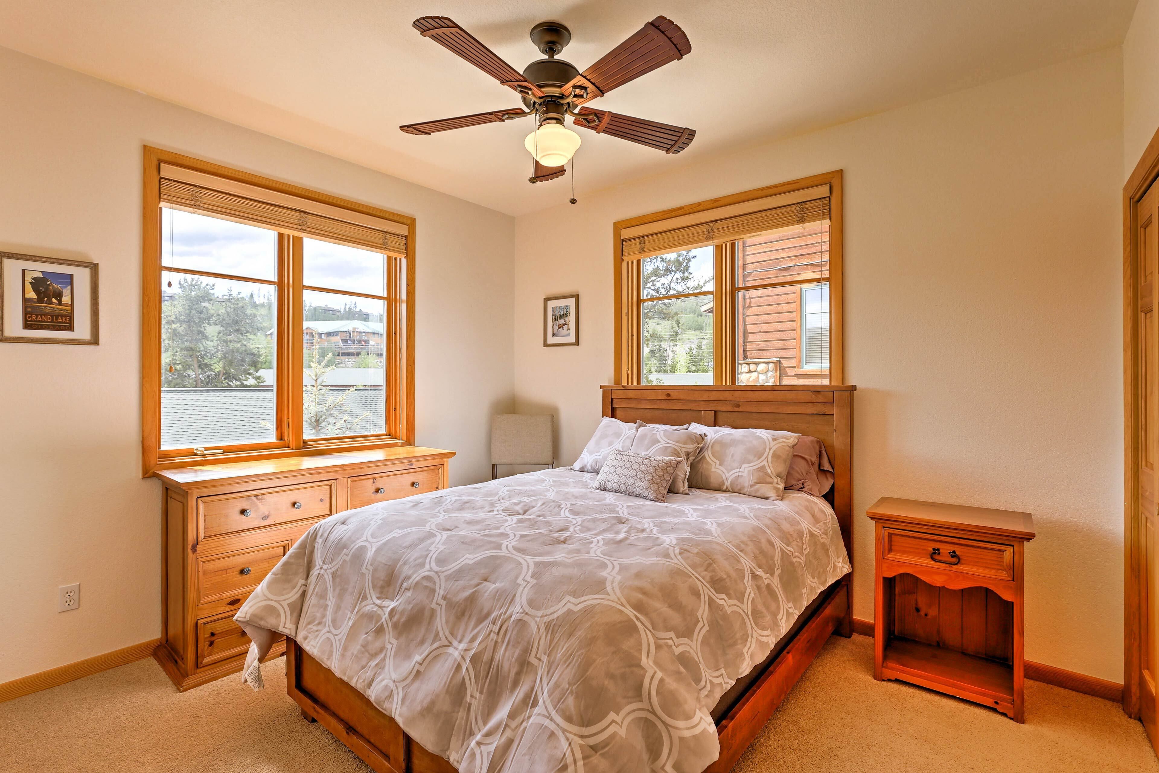 A bedroom with a bed, wooden nightstands, a ceiling fan, and large windows.