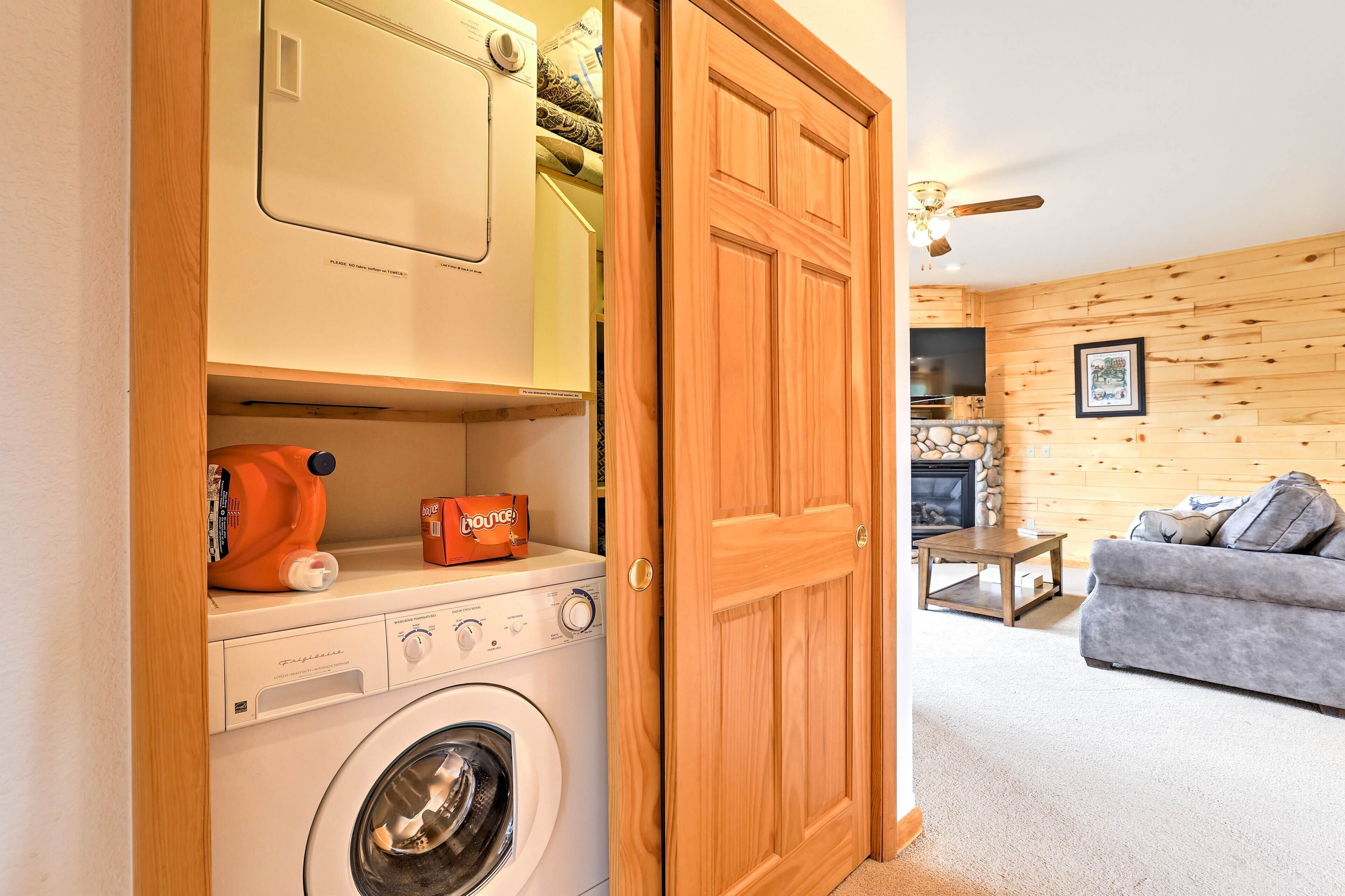 A laundry area with a washing machine, a dryer, and a shelf with a bottle of Bounce detergent.