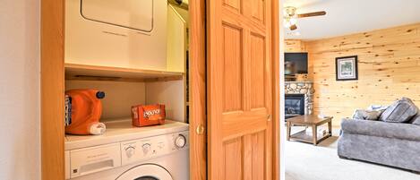 A laundry area with a washing machine, a dryer, and a shelf with a bottle of Bounce detergent.
