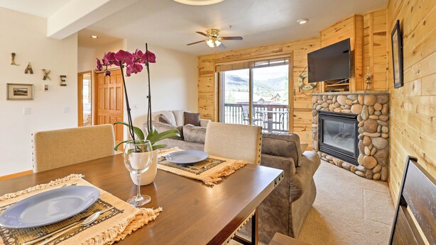 A dining area with a wooden table set for two, a fireplace, and a television mounted on the wall. - 7 Mi to National Park: Grand Lake Condo w/ Deck! (Grand Lake)