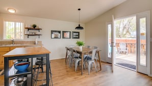 Cozinha moderna com ilha de madeira, banquetas e mesa de jantar com cadeiras. Há uma janela grande que oferece luz natural e vista para o quintal.