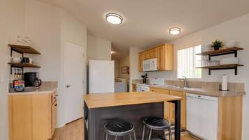 Een moderne keuken met houten kastjes, een centraal kookeiland met krukken, een magnetron en een vaatwasser.