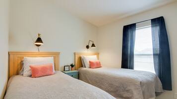 A room with two beds, each with a bedside table, a lamp, and a window with curtains.