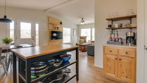 Uma cozinha moderna com armários de madeira, uma ilha central com espaço de armazenamento, uma área de jantar com cadeiras e uma sala de estar com sofá e mesa de centro.