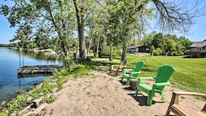 A lakeside area with a dock, green Adirondack chairs, and a grassy lawn.
