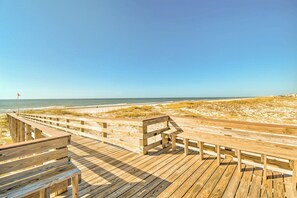 A wooden boardwalk leading to a beach with a flag in the distance. - Gulf Shores Condo w/ Resort-style Amenities! (Gulf Shores)