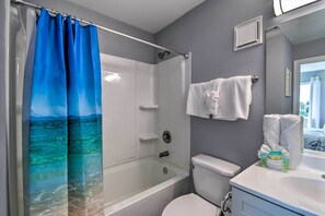 A bathroom with a bathtub, toilet, and a shower curtain with a sea view design.