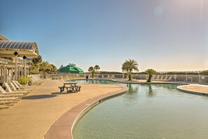 A swimming pool with lounge chairs and a covered area, surrounded by palm trees and a clear sky.