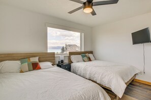 A bedroom with two beds, a ceiling fan, a TV, and a window with a view of buildings. - 3 Mi to Bear Lake & Marina! Spacious Group Getaway (Garden City)