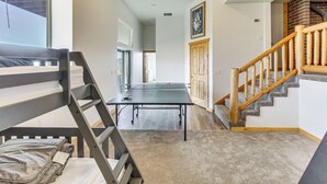 Een kamer met een stapelbed, een pingpongtafel, een trap met houten leuningen en uitzicht naar buiten door een raam.