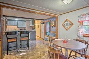 Cozinha com armários de madeira, área de jantar com mesa redonda e cadeiras, e um objeto decorativo na parede.