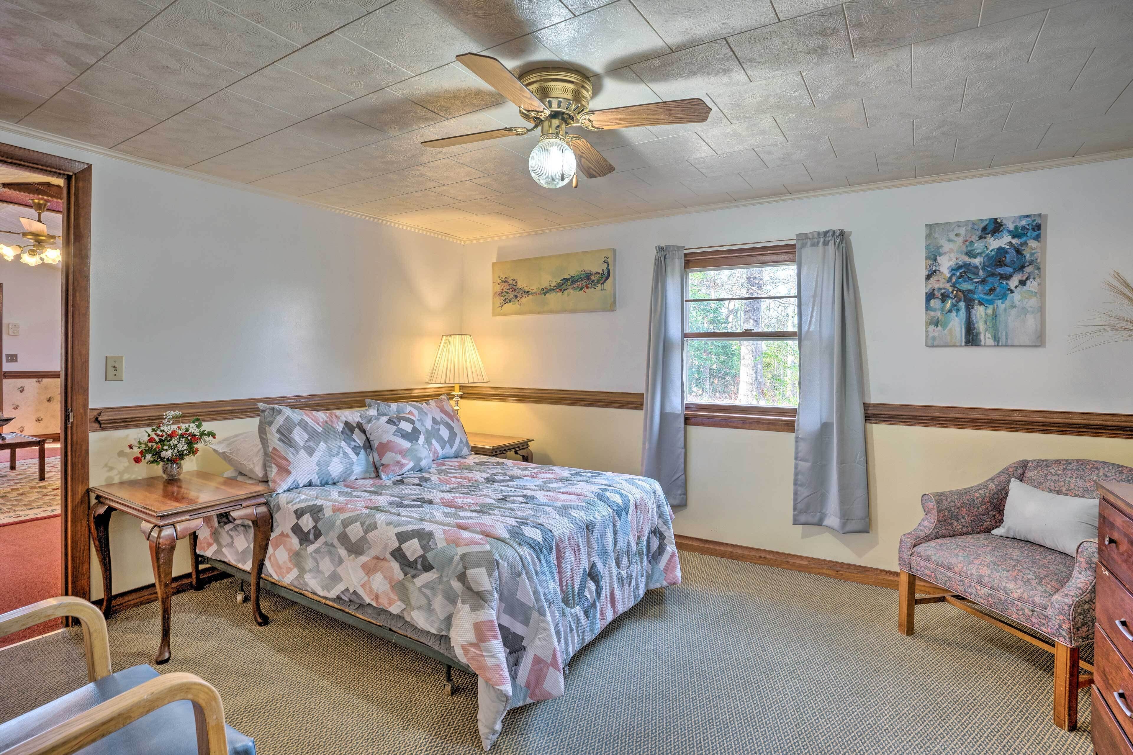 A bedroom with a bed, a wooden nightstand, a lamp, a chair, a dresser, and a ceiling fan.