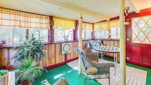 Una habitación acogedora con techo de madera, una mesa de comedor con sillas, una planta grande en maceta y una ventana con cortinas.