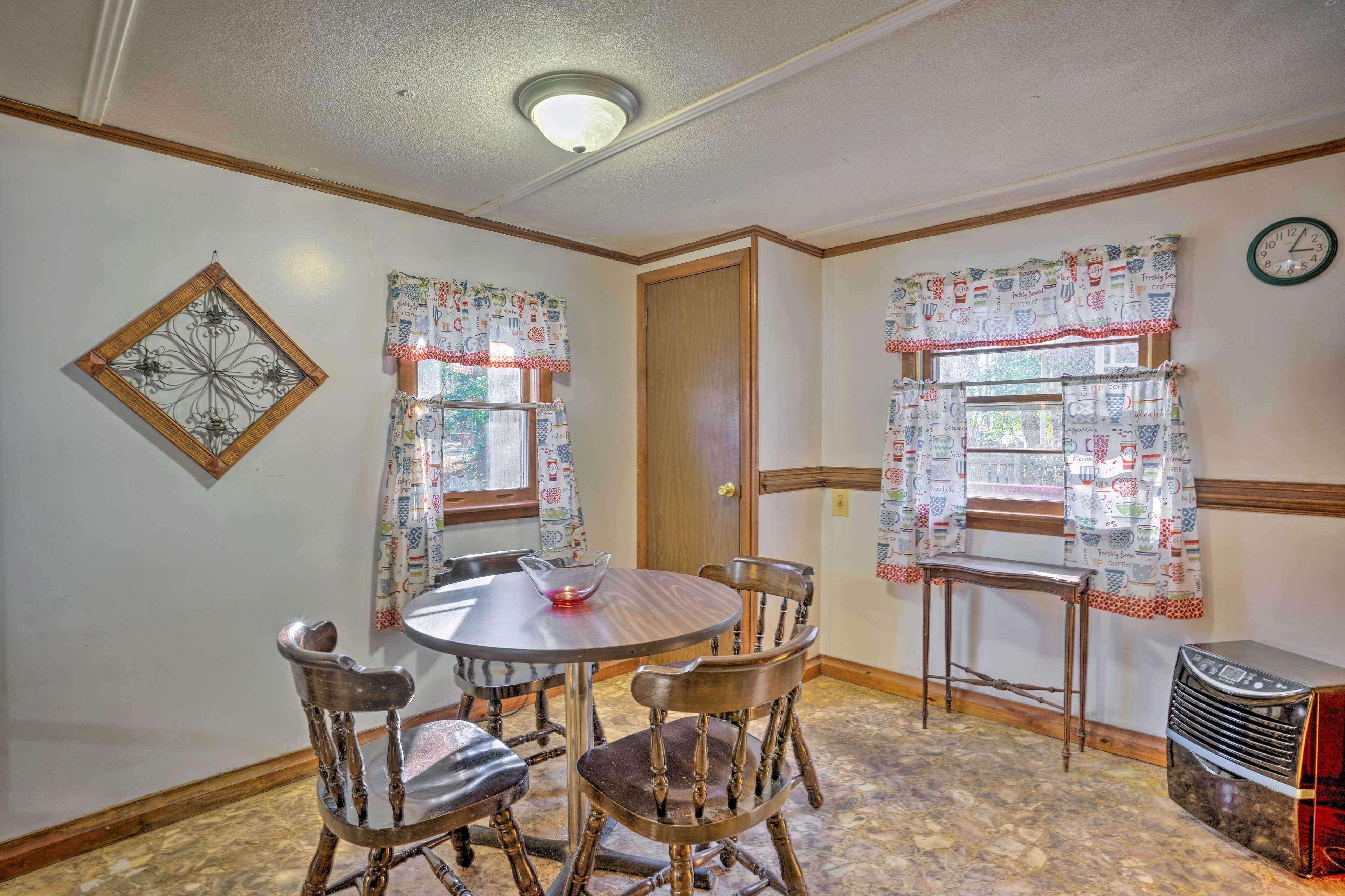 Un coin repas comprenant une table ronde, quatre chaises, un élément décoratif mural et des rideaux à motifs.