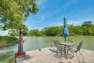 Um deck de madeira com uma mesa e cadeiras, um guarda-sol azul e um farol vermelho e branco.
