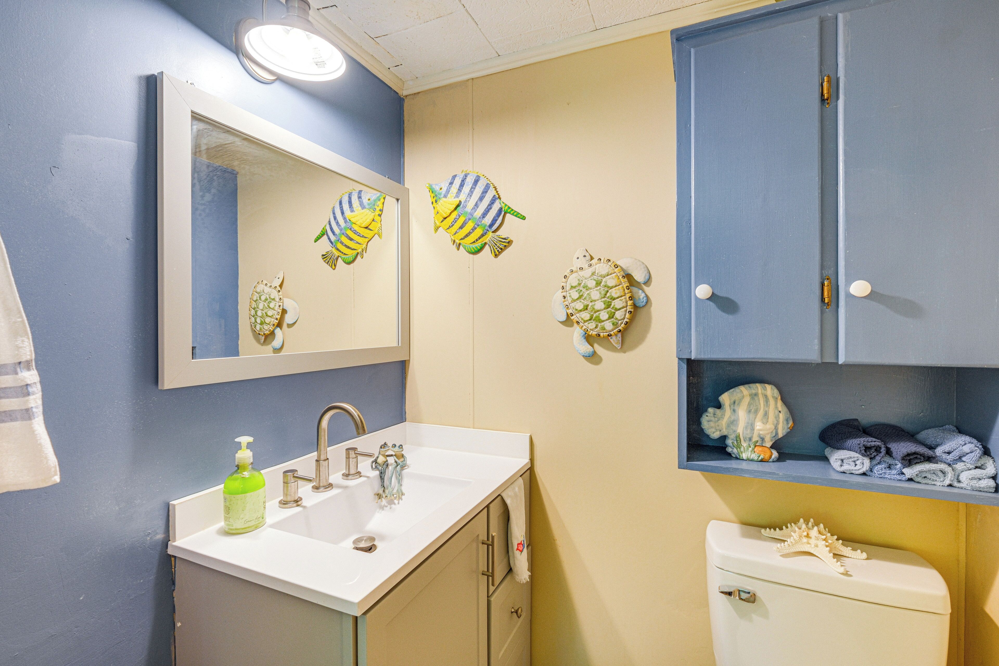 Un baño con lavamanos, espejo e inodoro. Se observan peces decorativos en la pared y un perchero para toallas.