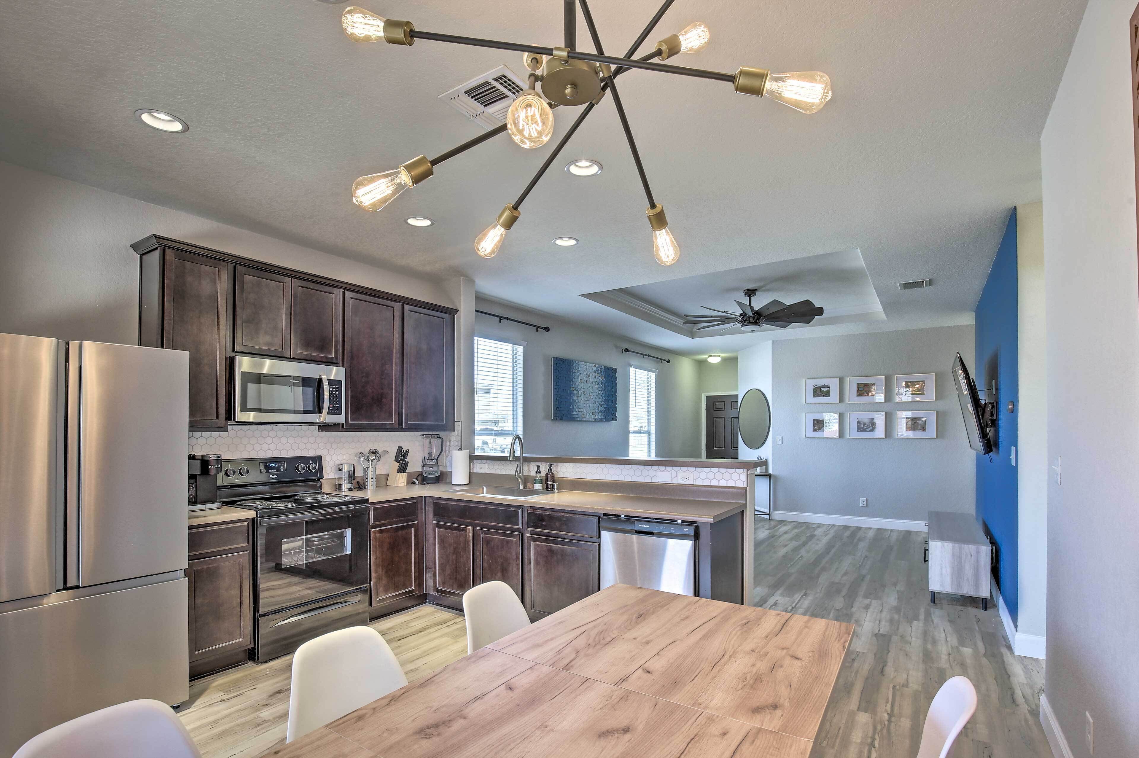 A modern kitchen with stainless steel appliances, a wooden dining table, and a ceiling light fixture.