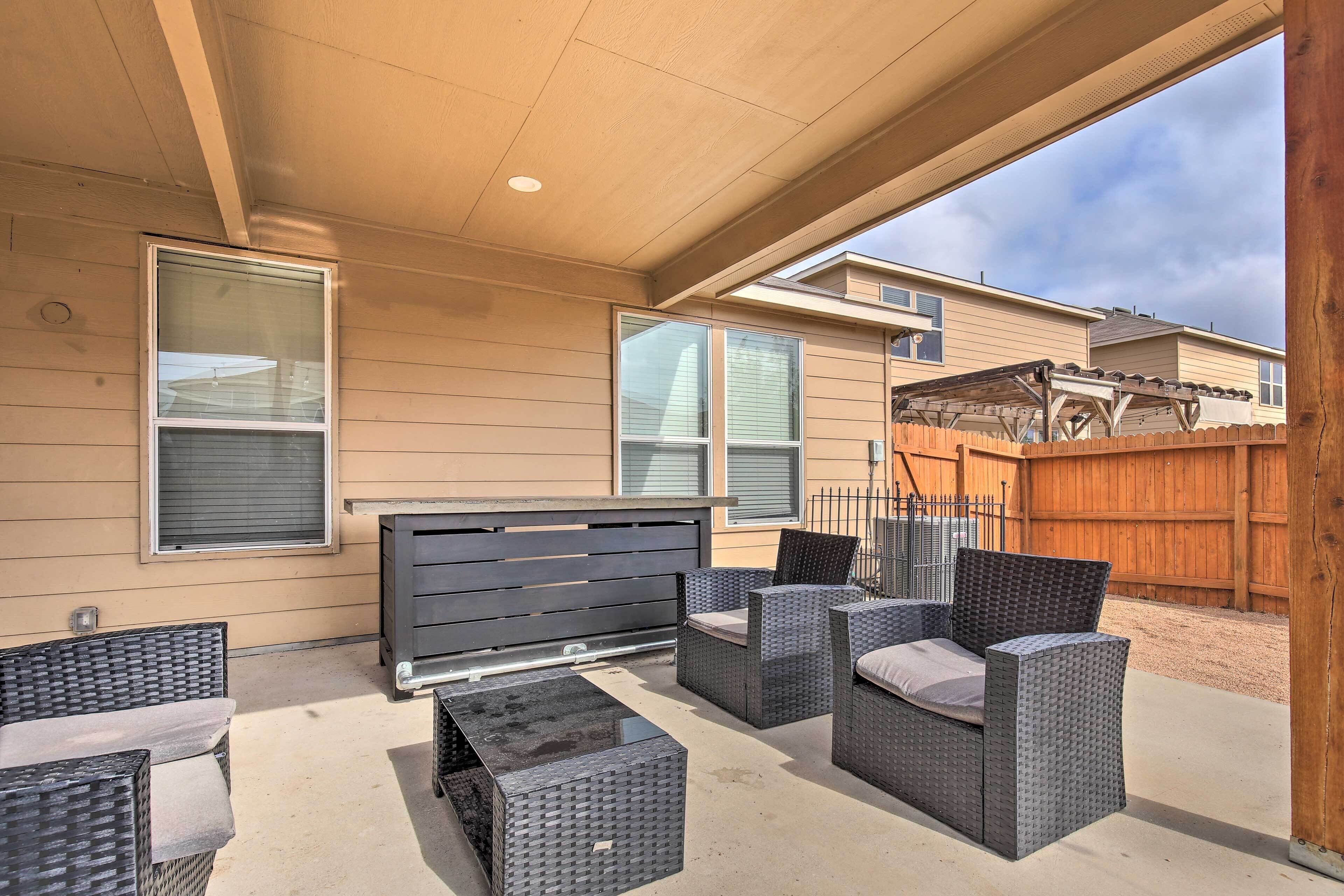 An outdoor patio area with wicker furniture, a black table, and a wooden fence in the background.