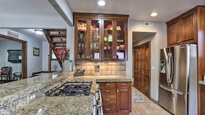 Una cocina con encimeras de granito, refrigerador de acero inoxidable, gabinetes de madera y horno empotrado.