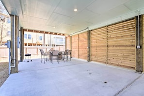 A covered patio area with a concrete floor, a table with chairs, and a wooden garage door.