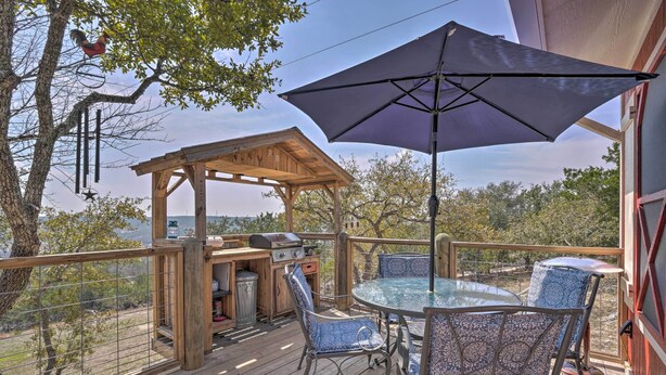 A wooden deck with a glass table and chairs, a barbecue area, and a pergola with a rooster decoration. - Kerrville Converted Barn Tiny Home w/ Kayaks! (Kerrville)