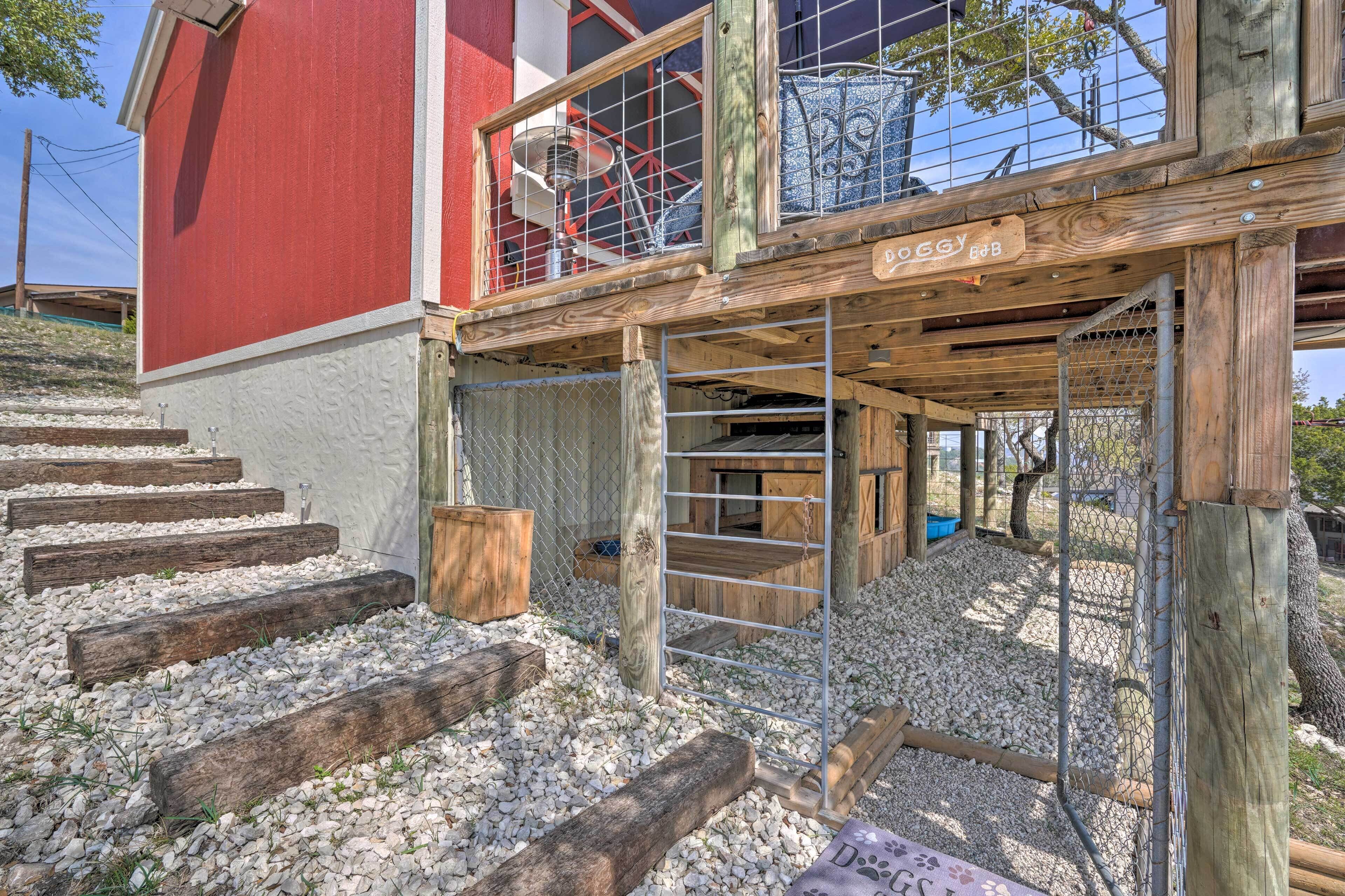 A wooden deck with a metal gate, steps leading to a red building, and a fenced area with gravel.