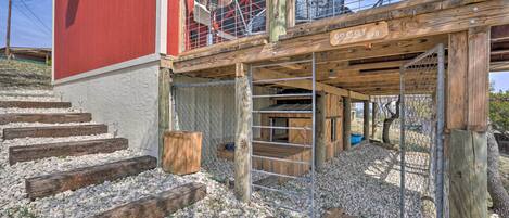 A wooden deck with a metal gate, steps leading to a red building, and a fenced area with gravel.