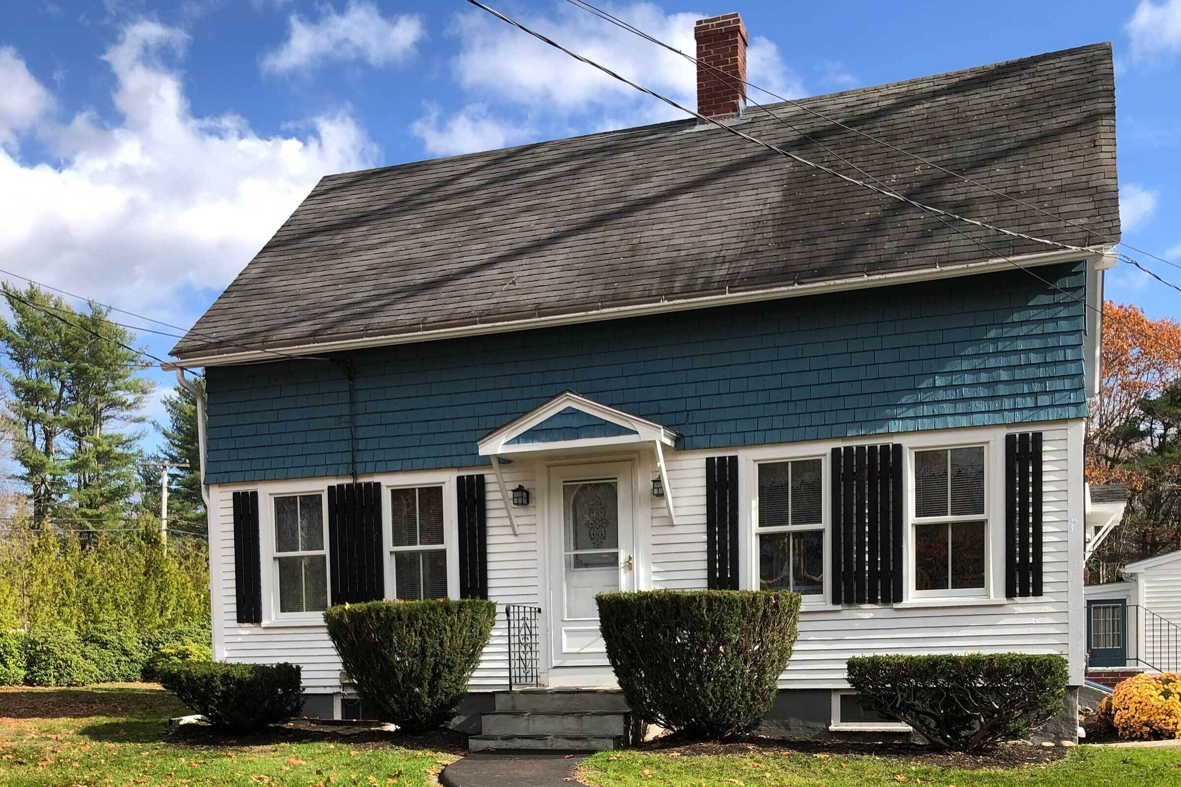 A two-story house with a dark blue exterior, white shutters, and a front porch with steps.