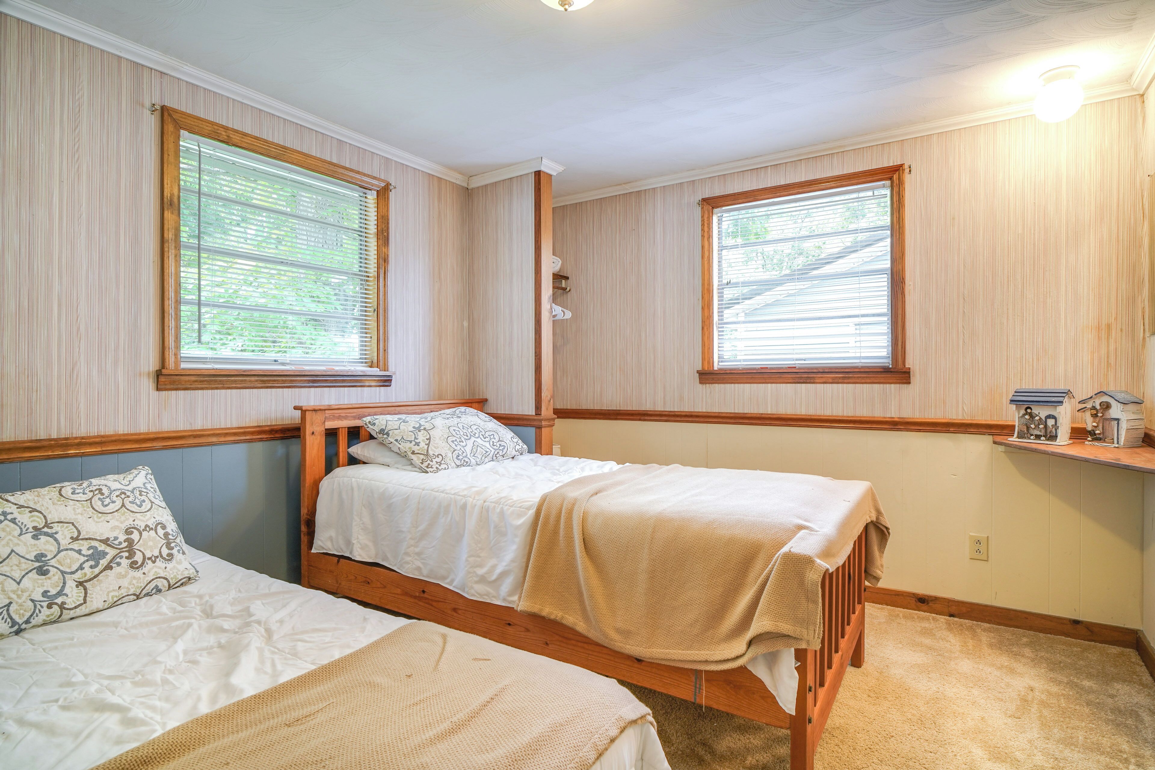 A bedroom with two single beds, wooden headboards, and large windows with blinds.