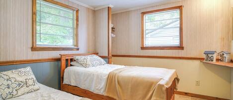 A bedroom with two single beds, wooden headboards, and large windows with blinds.