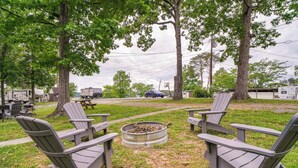Un terrain de camping avec des chaises Adirondack disposées autour d’un foyer, des camping-cars en arrière-plan et une table de pique-nique.