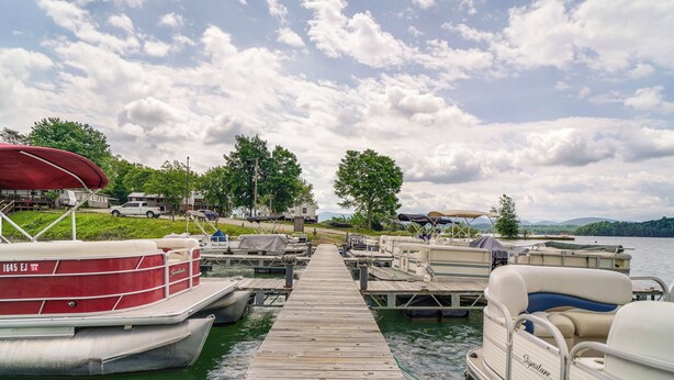 Un quai avec des bateaux, un espace abrité et une vue sur le lac et les collines.