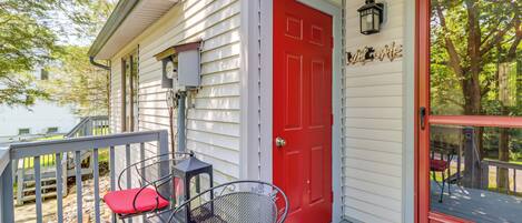 A porch with a red door, a metal chair with a red cushion, and a small table.