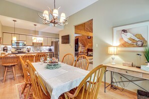 A dining area with a wooden table, chairs, and a chandelier. There is a kitchen in the background with modern appliances and wooden cabinets. - Walk to Dining! Townhome 1 Mi to Big Boulder Mtn (Lake Harmony)