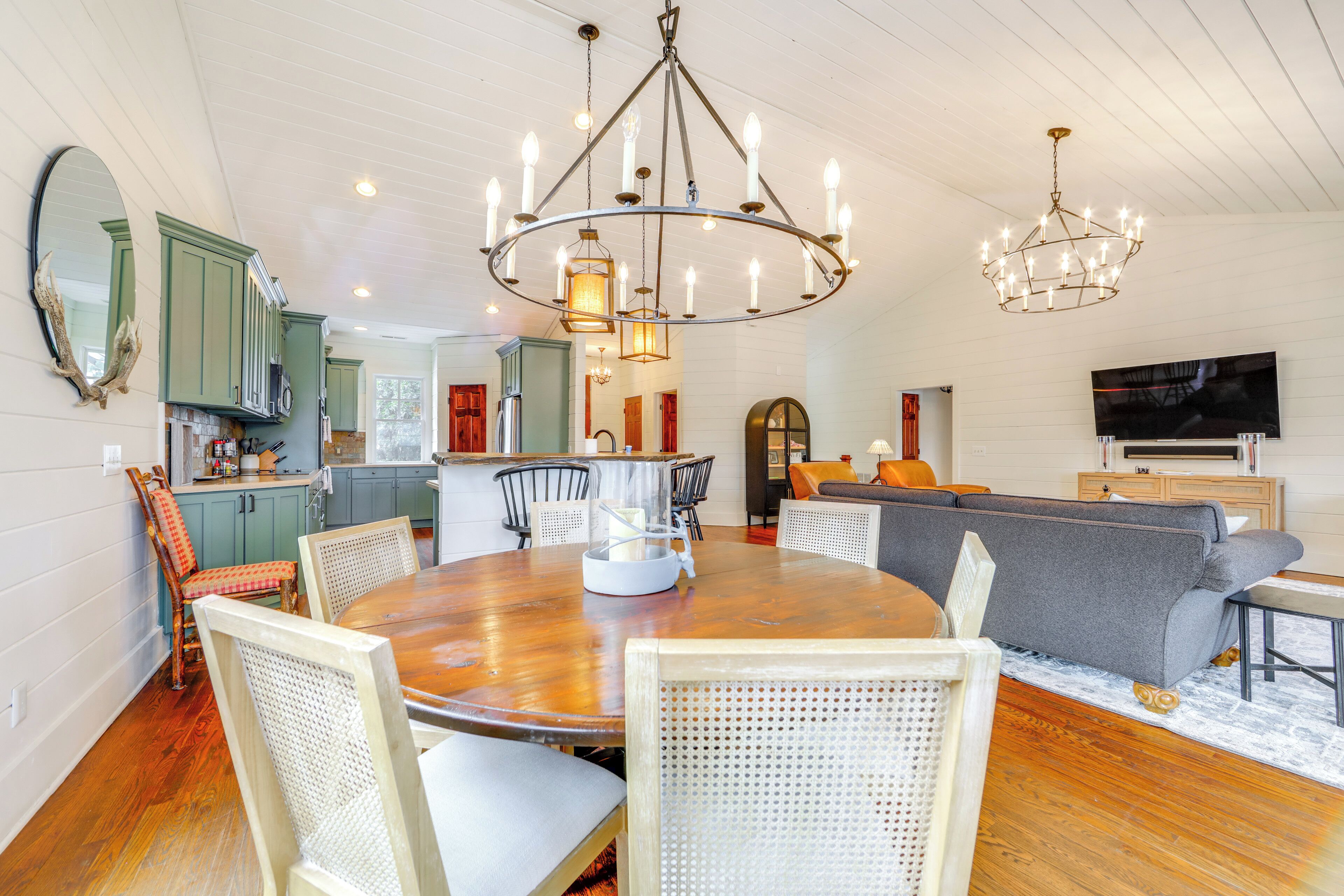 A spacious living room with a wooden dining table, wicker chairs, a grey sofa, and a chandelier.