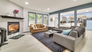 Una sala de estar moderna con chimenea, dos sofás, una mesa de centro y ventanas amplias.