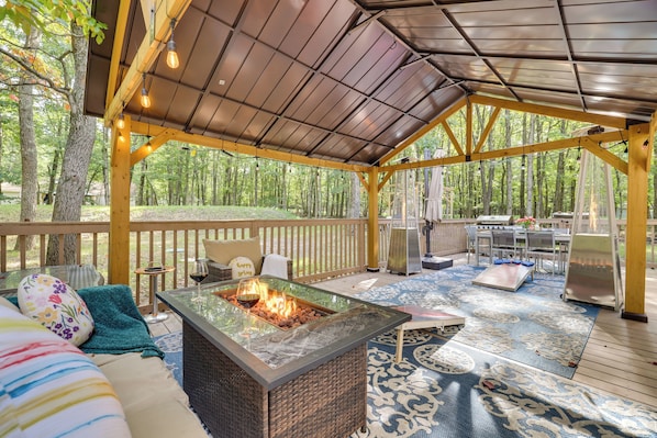 A covered outdoor patio with a fire feature, seating, and a grill area.