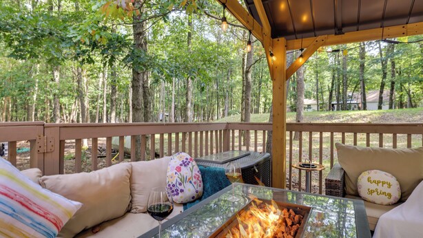 Un espacio de estar al aire libre cubierto con una mesa de vidrio, un hogar y vistas a un bosque.
