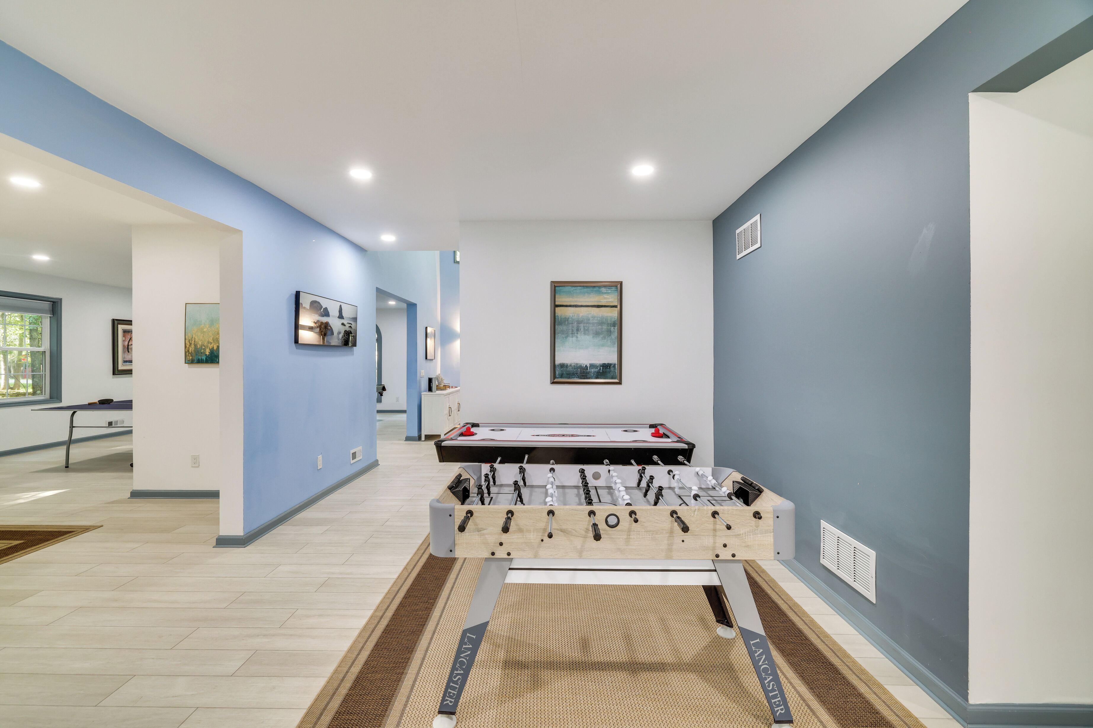 A room with a foosball table, a pool table, and artwork on the walls.