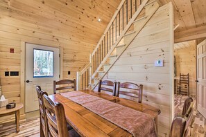 A wooden interior with a dining table, chairs, a staircase, and a door with a window.