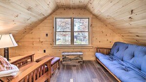 A cozy attic room with wooden walls, a large window, a blue sofa, a wooden bench, and a small table with a lamp. - Inviting Webb Lake Cabin w/ Mountain Views (Weld)