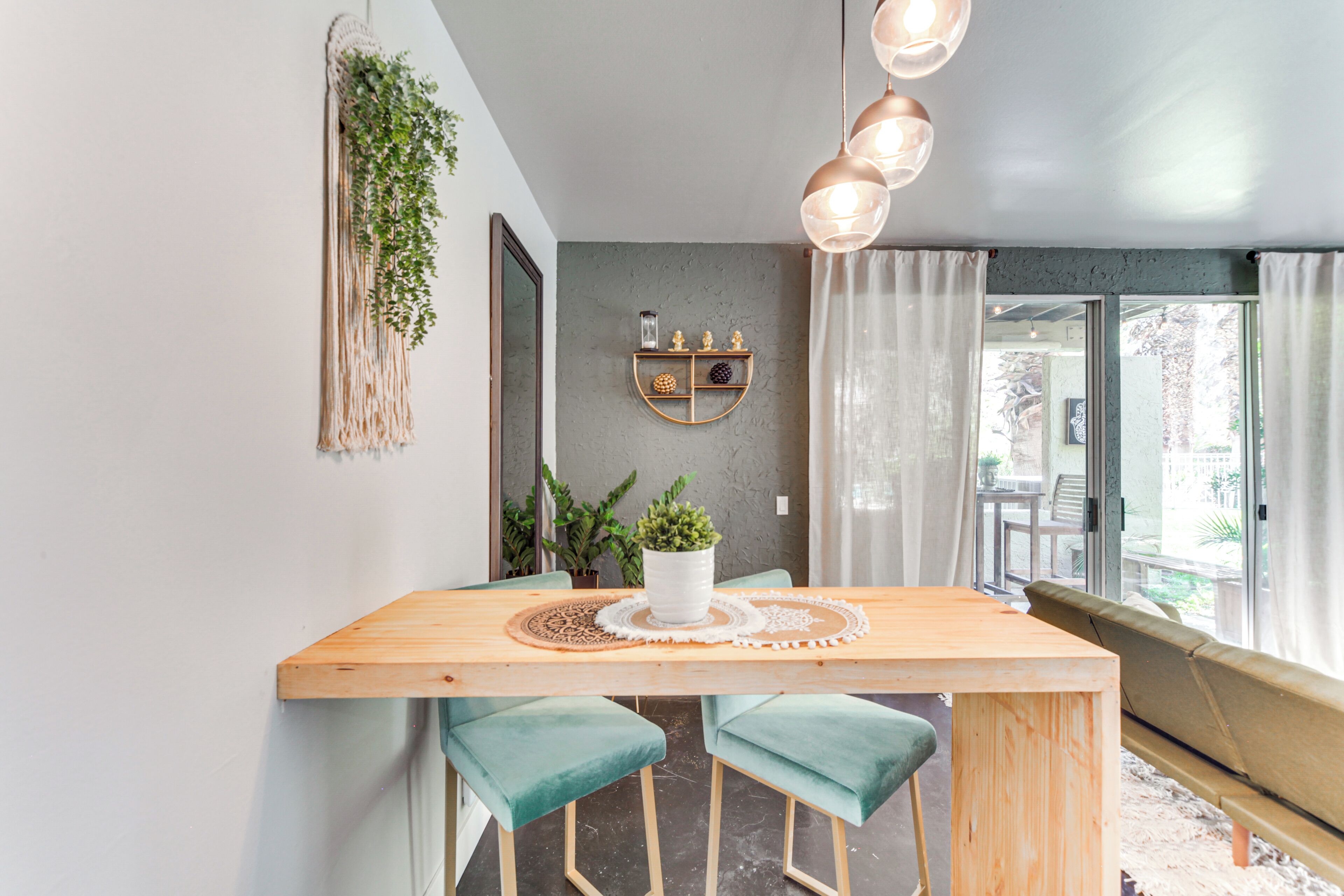 A modern dining area with a wooden table, teal chairs, a potted plant, and a pendant light.