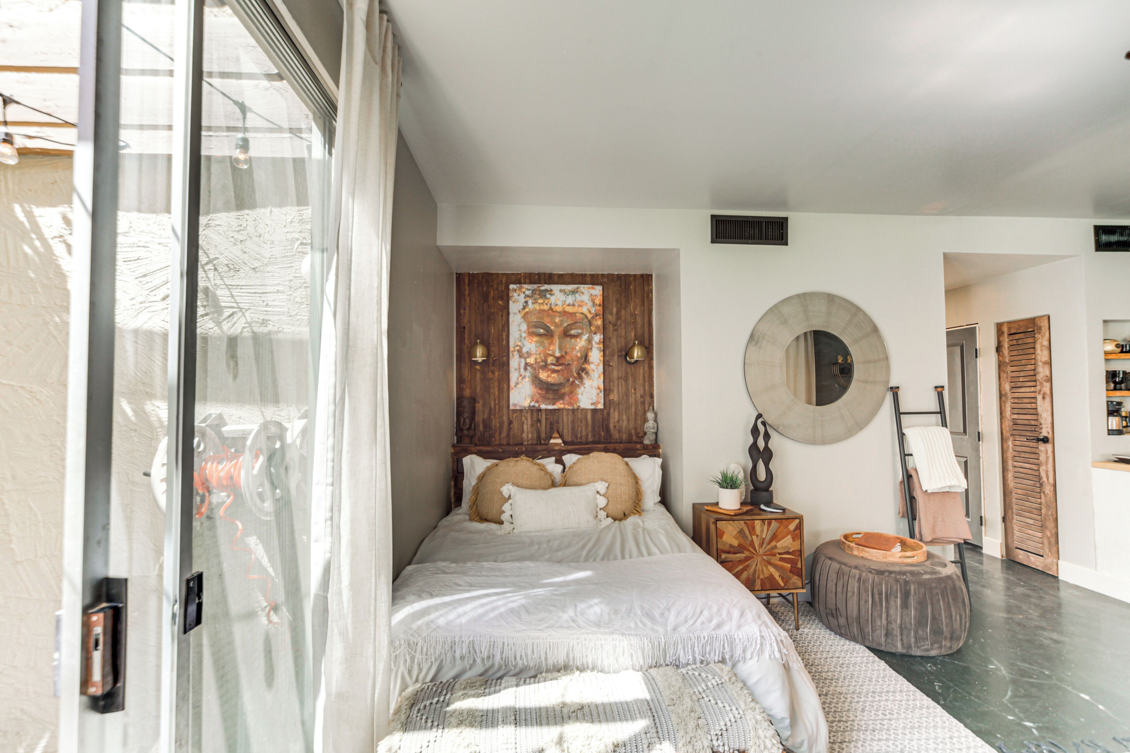 A bedroom with a bed, a round mirror, a wooden headboard, and a painting on the wall.