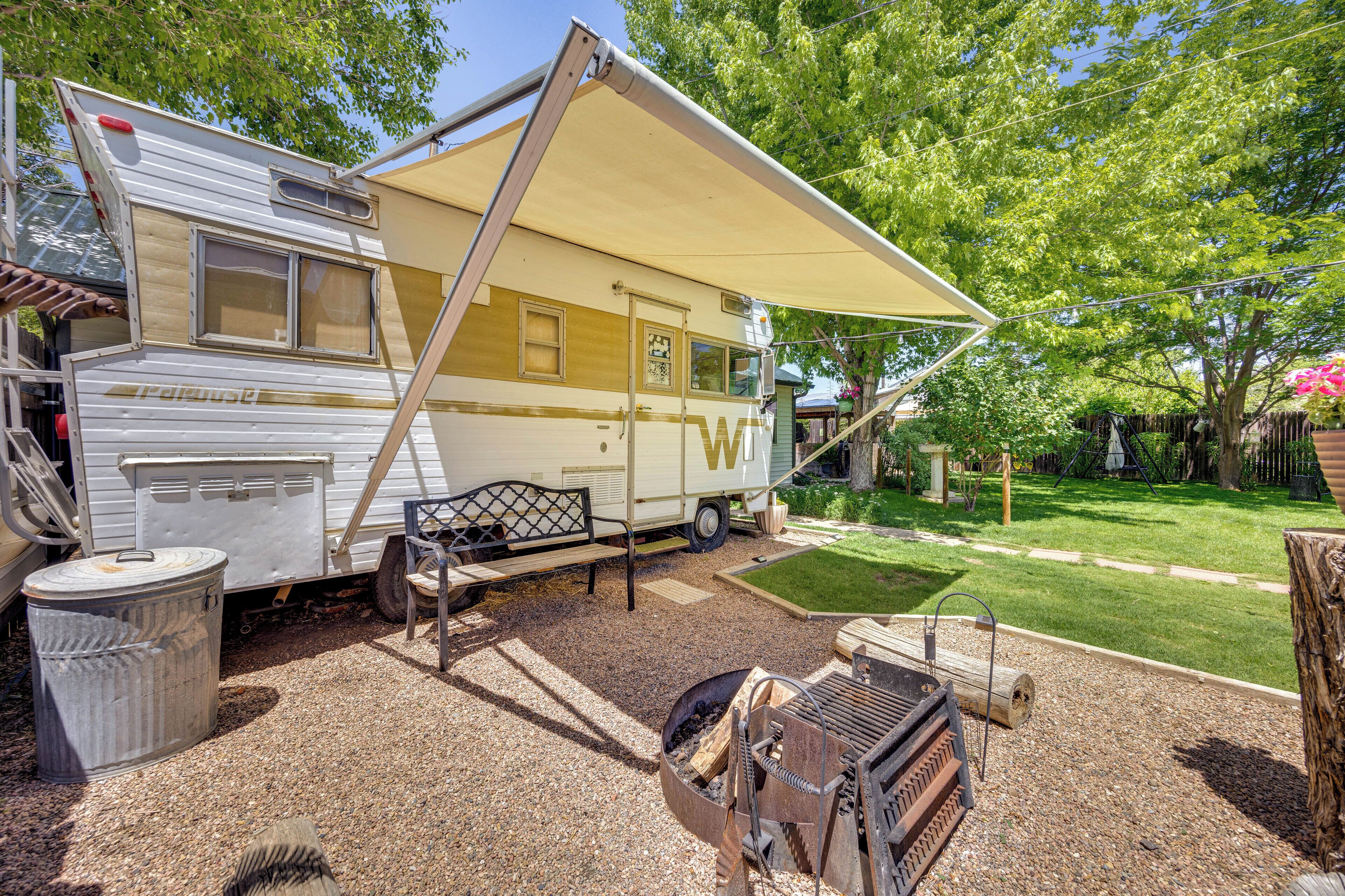 A recreational vehicle with a covered patio area, a grill, and a trash can.